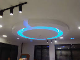 white drop ceiling with a large, round central feature illuminated by blue LED strip lighting, surrounded by various recessed spotlights and black track lightin
